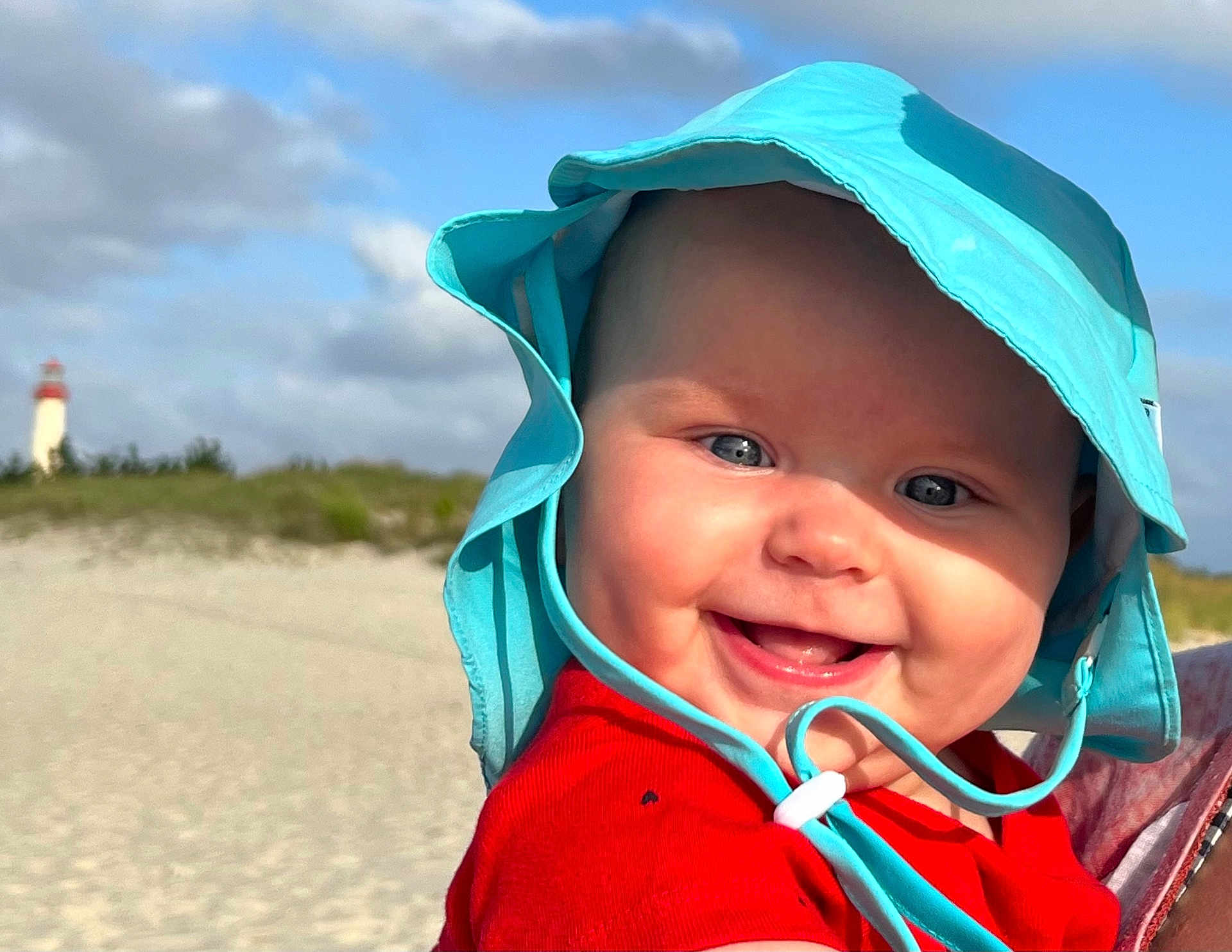 Josephine joined the competition — help win amazing prizes! baby, beach, blue_eyes, child, clouds, cute, daylight, happy, hat, headwear, infant, lighthouse, outdoor, portrait, red_clothing, sand, sky, smiling, sun_hat, vacation