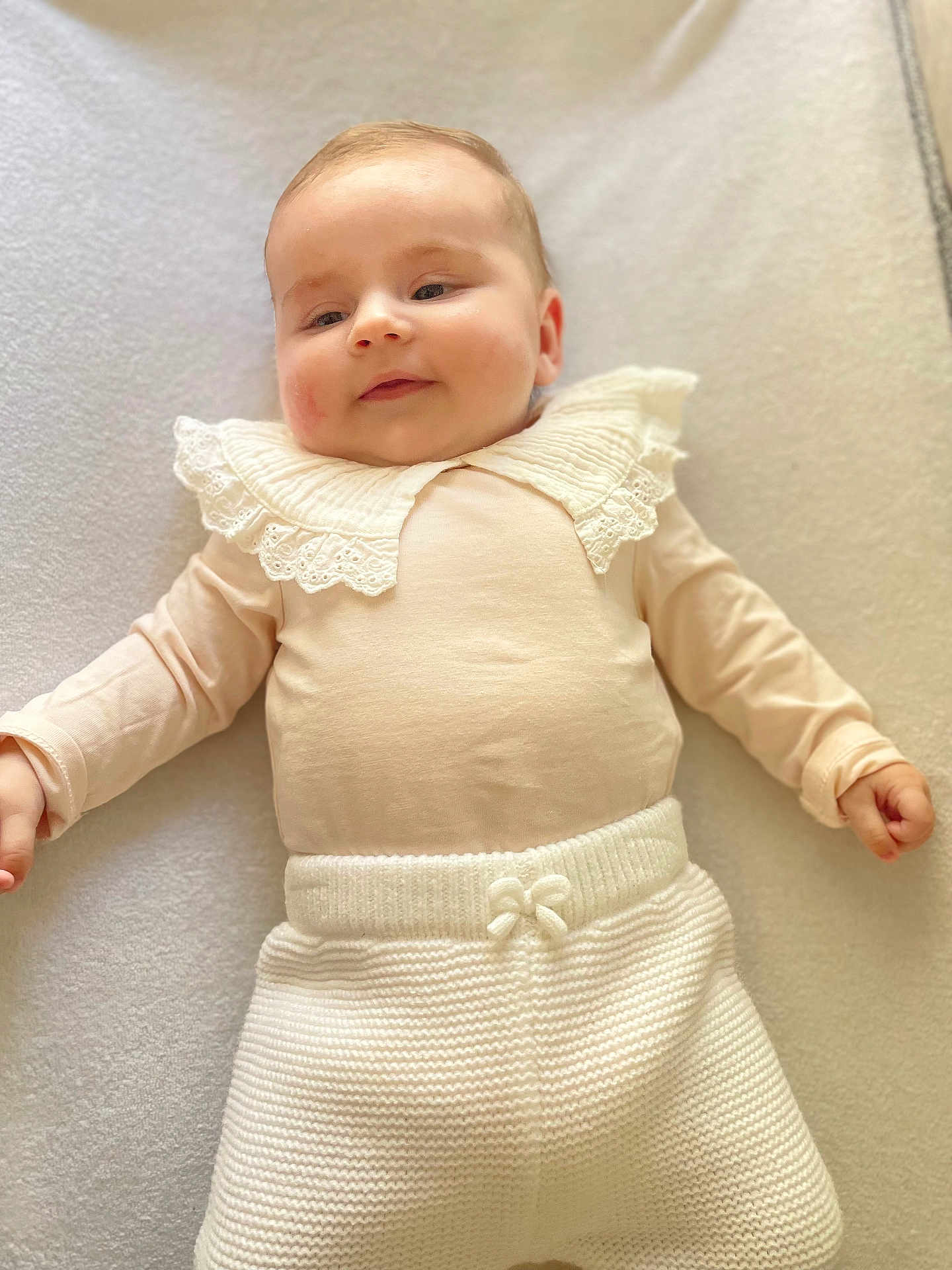 Joséphine participe au concours pour gagner de l'argent avec cette photo : baby, blanket, child, clothing, cute, face, hands, happy, head, indoor, infant, knitted_pants, lace_collar, lying_down, person, portrait, skin, smiling, soft_lighting, young