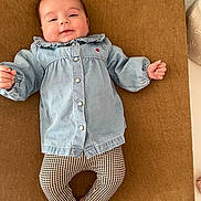 Joséphine participe au concours pour gagner de l'argent avec cette photo : baby, brown_background, casual_wear, child, clothing, comfortable, cute, denim_jacket, feet, happy, indoors, infant, lying_down, patterned_leggings, portrait, relaxed, small_hands, smiling, soft_lighting, young_child