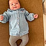 baby, brown_background, casual_wear, child, clothing, comfortable, cute, denim_jacket, feet, happy, indoors, infant, lying_down, patterned_leggings, portrait, relaxed, small_hands, smiling, soft_lighting, young_child