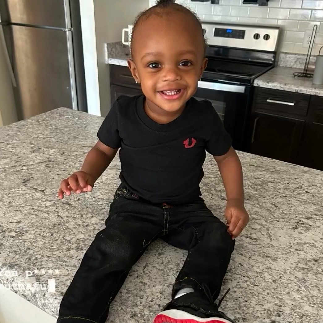 Jahmarii joined the competition — help win amazing prizes! toddler, child, smiling, sitting, kitchen, countertop, black_clothing, jeans, sneakers, modern_kitchen, appliances, refrigerator, oven, microwave, happy, portrait, indoor, person, cute, young_child