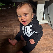 Kash joined the competition — help win amazing prizes! baby, child, smiling, happy, sitting, floor, wooden_floor, hoodie, nike, black_clothing, indoor, cute, portrait, face, blue_eyes, infant, one_person, casual_clothing, young_child, barefoot