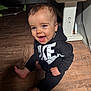 baby, child, smiling, happy, sitting, floor, wooden_floor, hoodie, nike, black_clothing, indoor, cute, portrait, face, blue_eyes, infant, one_person, casual_clothing, young_child, barefoot