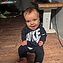 Kash is registered to the contest to win money with this photo: baby, child, smiling, sitting, floor, indoor, nike, clothing, blue_eyes, happy, person, footwear, wooden_floor, toy, walker, table, home, cute, portrait, infant