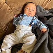 Hugo Rodriguez joined the competition — help win amazing prizes! baby, child, infant, blue_shirt, suspenders, white_pants, brown_couch, blanket, footwear, shoes, portrait, indoor, cute, relaxed, clothing, face, person, sitting, young_child, casual