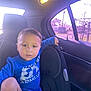 toddler, child, car_interior, car_seat, blue_shirt, diaper, window, sunlight, seatbelt, rear_seat, person, young_child, casual_clothing, daylight, automobile, headrest, seat, portrait, indoors, curious_expression