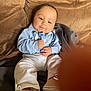 baby, child, infant, blue_shirt, suspenders, white_pants, shoes, couch, blanket, brown, indoor, portrait, cute, face, hands, seated, expression, cozy, soft_lighting, casual