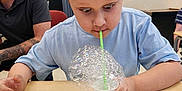 Tyler Jr. joined the competition — help win amazing prizes! child, boy, bubbles, foam, straw, cup, table, classroom, concentration, play, learning, adult, person, indoor, short_hair, casual_clothing, expression, fun, education, activity