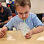 child, boy, bubbles, foam, straw, cup, table, classroom, concentration, play, learning, adult, person, indoor, short_hair, casual_clothing, expression, fun, education, activity