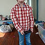 child, boy, smile, plaid_shirt, jeans, tablet, indoor, wooden_floor, shoes, photographs, toys, plastic_container, clutter, casual_clothing, home, person, portrait, happy, standing, technology