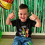 balloon, birthday, boy, casual_clothing, celebration, child, cute, dinosaur, floor, green_streamers, hair, happy, indoor, jeans, party, portrait, smiling, thumbs_up, tshirt, young