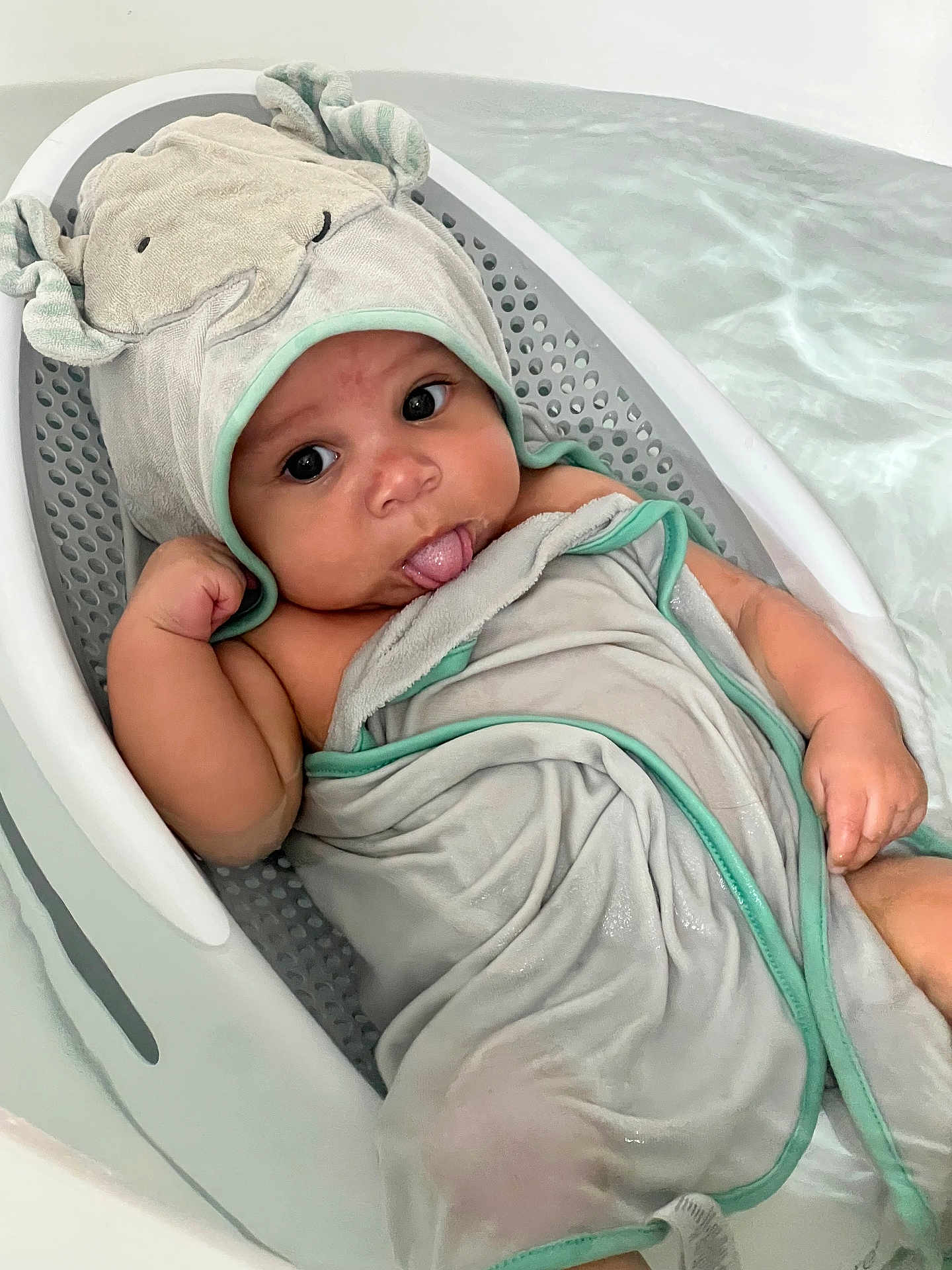 Zaire is registered to the contest to win money with this photo: baby, bathtub, towel, hood, playful, water, infant, bath, cute, child, wrapped, skin, tongue, expression, relaxing, indoor, soft, smiling, person, bathroom