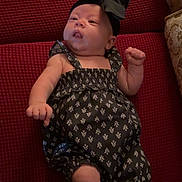 Lilah joined the competition — help win amazing prizes! baby, infant, black_bow, romper, patterned_clothing, red_couch, textured_fabric, cute, indoors, furniture, headband, small_fists, relaxed, lying_down, child, adorable, person, comfort, home, portrait