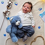 Ezio a rejoint le concours — aidez-le/la à gagner de superbes lots ! baby, baby_clothing, blue_petal, child, cotton_branch, cozy, cute, decor, glowing_lamp, happy, heart_shape, indoor, lying_down, plush_toy, portrait, smiling_baby, soft_mat, star_pattern_pants, teddy_bear, white_shirt