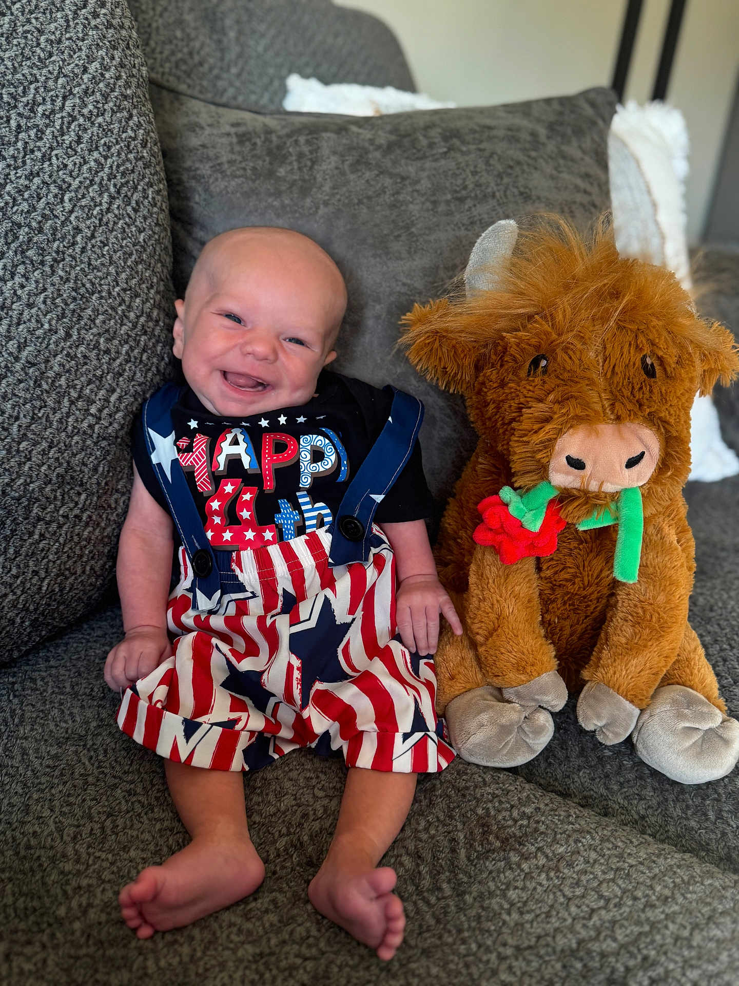 Braxton is registered to the contest to win money with this photo: baby, smiling, child, stuffed_animal, plush_toy, couch, gray_couch, clothing, happy, indoors, portrait, sitting, cute, toy, soft_toy, infant, fabric, decor, funny, comfort