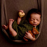 Tatum joined the competition — help win amazing prizes! newborn, baby, sleeping, teddy_bear, heart, green_outfit, brown_background, fabric, cozy, cute, infant, portrait, resting, child, soft_lighting, wrapped, peaceful, tiny_feet, handheld_toy, closeup