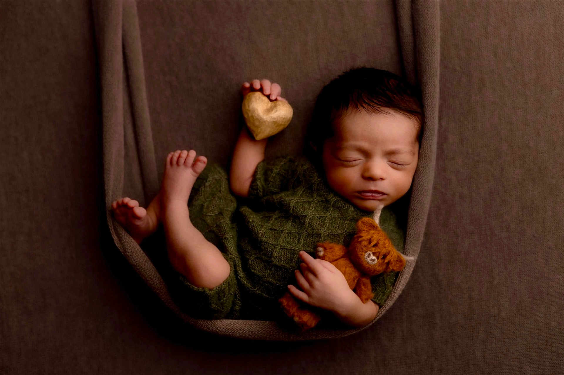 Tatum joined the competition — help win amazing prizes! newborn, baby, sleeping, teddy_bear, heart, green_outfit, brown_background, fabric, cozy, cute, infant, portrait, resting, child, soft_lighting, wrapped, peaceful, tiny_feet, handheld_toy, closeup