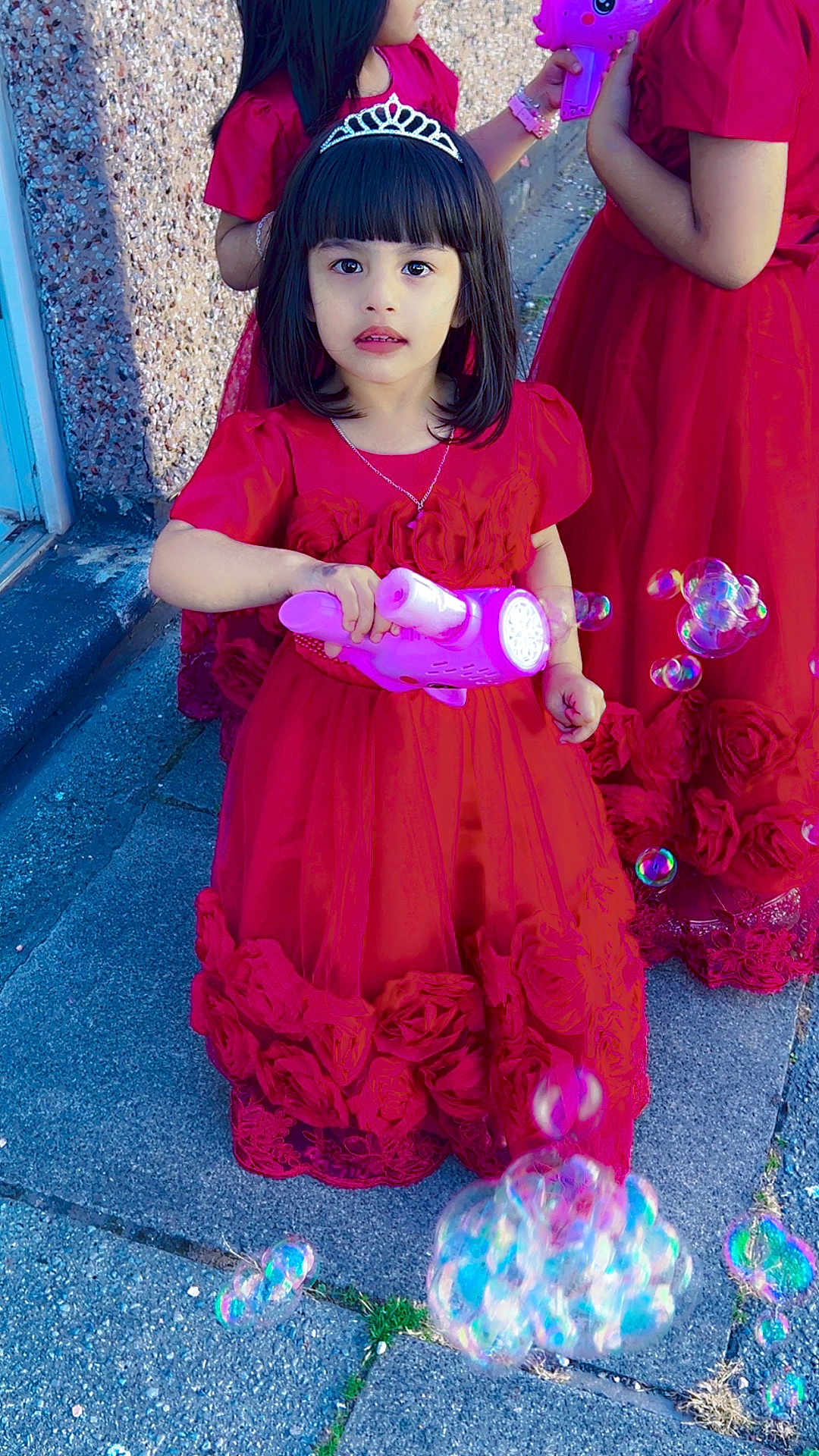Aima joined the competition — help win amazing prizes! child, girl, red_dress, tiara, bubble_gun, bubbles, outdoor, sidewalk, playing, party, celebration, toy, dress, flower_details, hand, face, person, happy, friends, sunlight