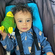 Abiel is registered to the contest to win money with this photo: toddler, child, car_seat, plush_toy, parrot_toy, curly_hair, blue_onesie, safety_harness, indoor, smiling, face, person, cute, baby, seatbelt, holding, toy, infant, young_child, portrait