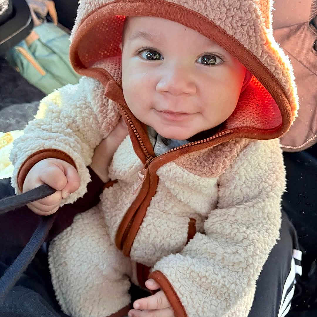 Mateo is registered to the contest to win money with this photo: baby, bonnet, cap, clothing, coat, face, happy, hat, head, hood, hoodie, jacket, knitwear, person, photography, portrait, sitting, smile, sweater, sweatshirt