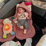 Arianna is registered to the contest to win money with this photo: baby, infant, playpen, blanket, plush_toy, pink_clothing, pacifier, sherpa, animal_toy, soft_toys, sleepwear, cute, child, indoors, resting, comfort, small_hands, patterned_pants, toy_light, baby_care
