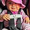 baby, child, infant, car_seat, safety_harness, pink_hat, striped_clothing, smiling, portrait, indoor, vehicle, seated, close_up, face, hands, baby_clothing, sun_hat, safety_sensor, happy, photography