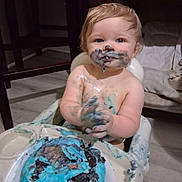 Wyatt is registered to the contest to win money with this photo: baby, child, high_chair, cake, blue_frosting, messy, eating, smiling, portrait, indoor, kitchen, chair, food, dessert, birthday, cream, hands, face, blond_hair, happy