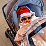 Mélodie a rejoint le concours — aidez-le/la à gagner de superbes lots ! baby, stroller, blanket, santa_hat, sunglasses_filter, indoor, floor, tile, winter_clothing, cartoon_snowman, cute, child, person, holiday, festive, warm, cozy, plastic_cover, seat, toy