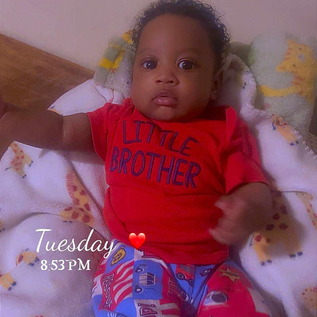 Sincere is registered to the contest to win money with this photo: baby, blanket, child, colorful_pants, cozy, curious, cute, eyes, face, giraffe_pattern, home, indoors, infant, lying_down, person, red_shirt, sleepwear, text_overlay, toddler, young_child