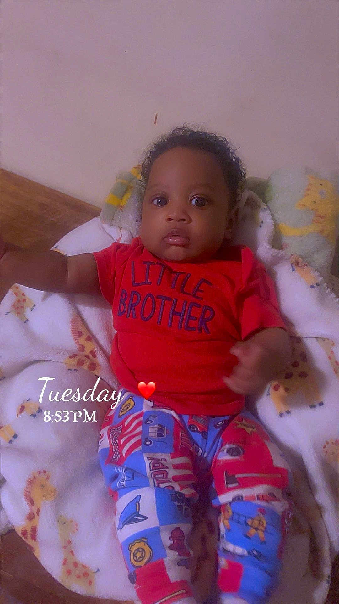 Sincere is registered to the contest to win money with this photo: baby, child, infant, red_shirt, colorful_pants, blanket, giraffe_pattern, face, eyes, curious, indoors, lying_down, person, cute, young_child, home, cozy, sleepwear, toddler, text_overlay