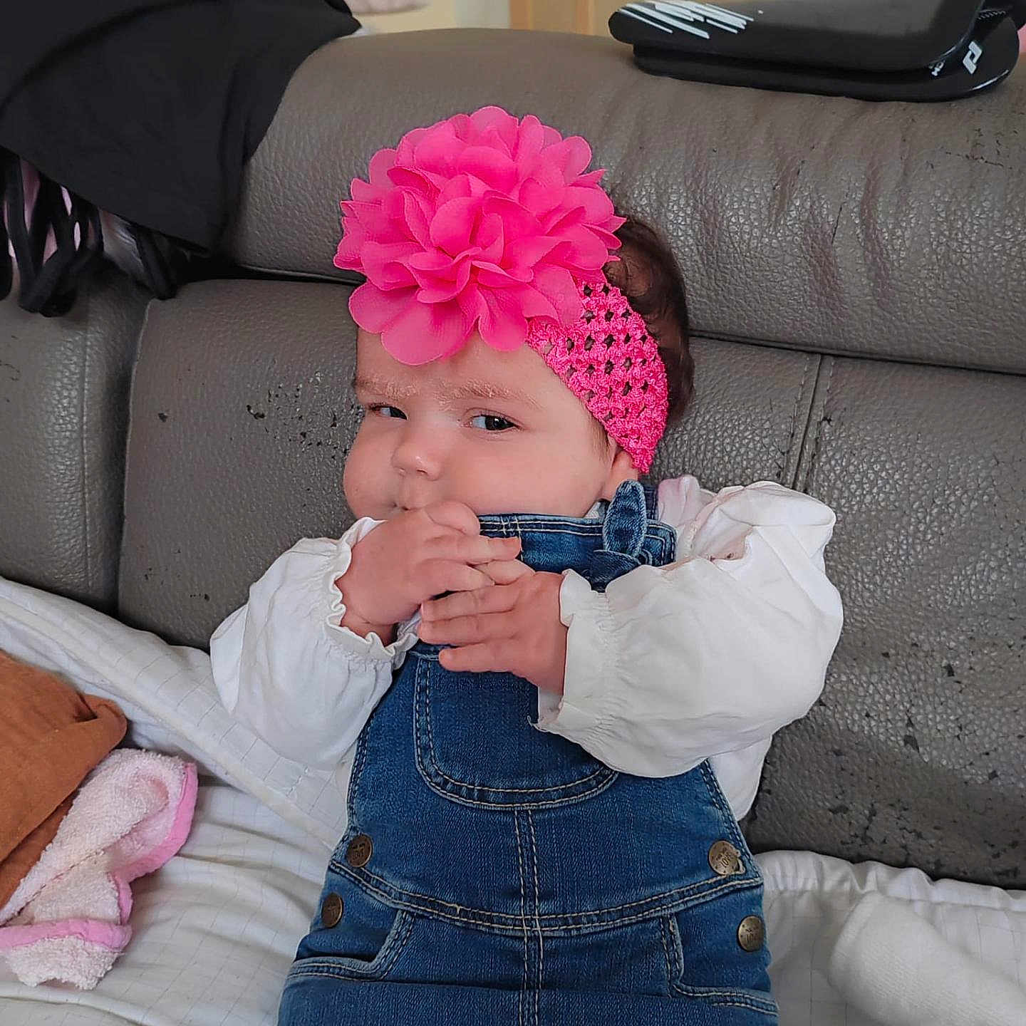 Zaÿna participe au concours pour gagner de l'argent avec cette photo : baby, blanket, chewing, child, clothing, couch, cozy, cute, denim_overalls, fabric, flower_headband, hands, home, indoors, infant, mischievous, pink_headband, portrait, seated, white_shirt