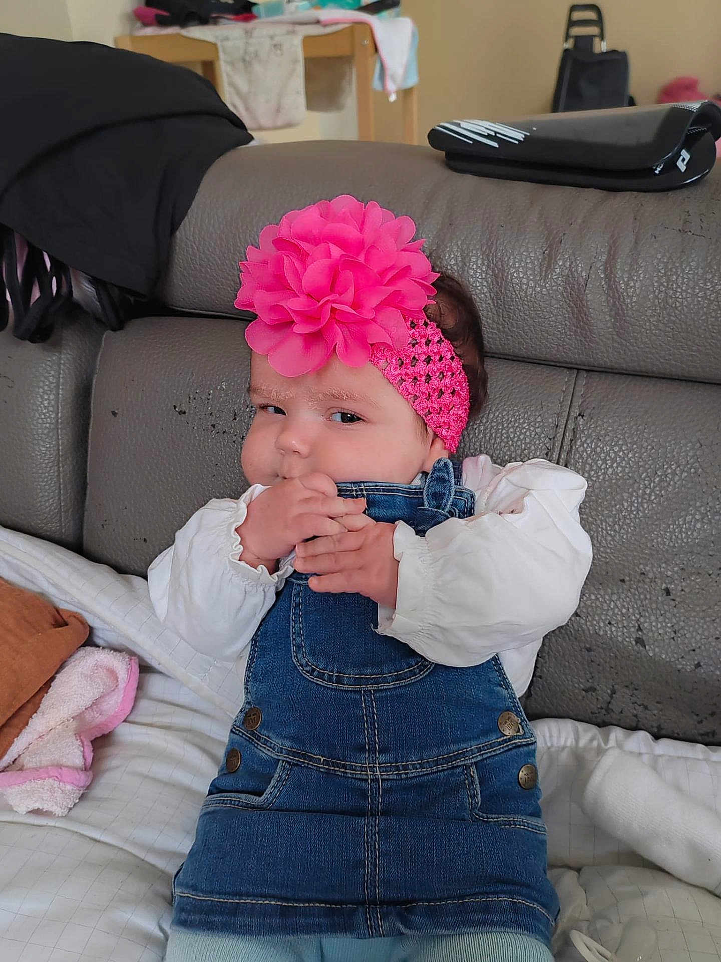 Zaÿna participe au concours pour gagner de l'argent avec cette photo : baby, infant, denim_overalls, pink_headband, flower_headband, chewing, couch, blanket, white_shirt, indoors, child, cute, mischievous, hands, fabric, home, seated, cozy, clothing, portrait