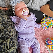 Zaÿna participe au concours pour gagner de l'argent avec cette photo : baby, sleeping, pacifier, headband, flower, purple_clothing, infant, blanket, pillow, soft_texture, cozy, child, indoors, resting, cute, peaceful, toddler, person, closeup, relaxation