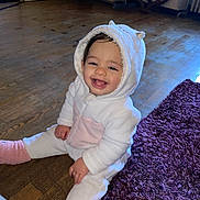Kenza participe au concours pour gagner de l'argent avec cette photo : baby, child, smiling, hooded_onesie, white_clothing, pink_booties, sitting, wooden_floor, purple_rug, indoor, happy, cute, face, person, infant, cozy, warm_clothing, playful, young_child, adorable