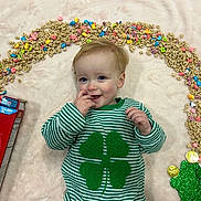 Theodore joined the competition — help win amazing prizes! child, baby, infant, smile, green_sweater, four_leaf_clover, cereal, lucky_charms_box, marshmallows, blanket, laying_down, portrait, happy, hand_to_mouth, gold_coins, colorful, toy, striped_clothing, indoor, cute