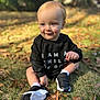 toddler, child, grass, autumn_leaves, black_sweatshirt, sneakers, outdoor, smiling, blue_eyes, light_hair, sitting, nature, young_child, casual_clothing, daylight, cute, playful, portrait, happy, seasonal