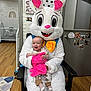 baby, easter_bunny, costume, indoor, nursery, crib, wooden_floor, blanket, pink, child, smiling, person, family_photos, chair, mascot, happy, toy, decor, people, candid