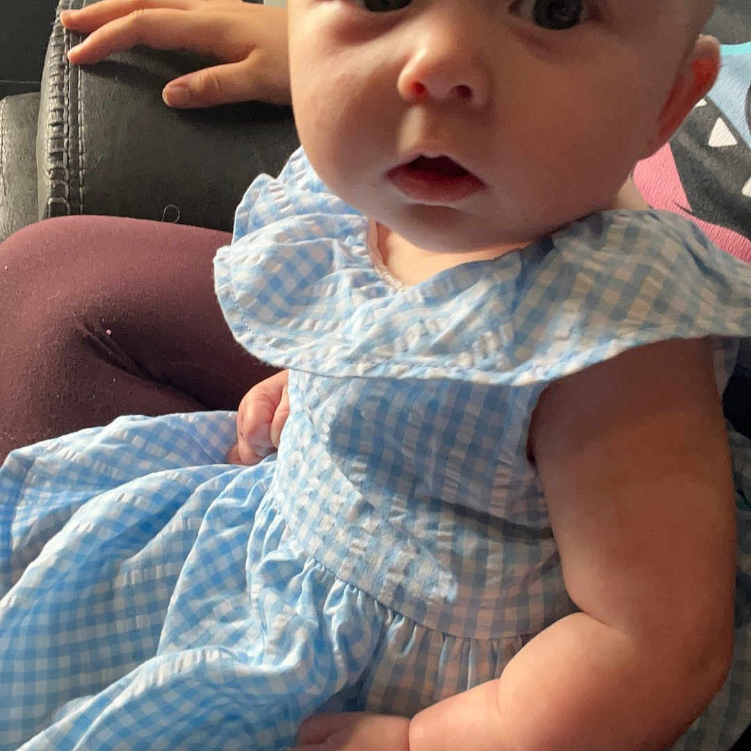 Lilly is registered to the contest to win money with this photo: baby, bodypart, chair, clothing, couch, cushion, dress, face, finger, furniture, hand, happy, head, homedecor, newborn, pants, person, photography, portrait, sitting
