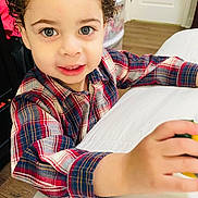 Joseph Rivas is registered to the contest to win money with this photo: child, toddler, curly_hair, plaid_shirt, indoor, face, blue_eyes, hand, wooden_floor, bed, white_bedspread, smiling, person, young_child, cute, portrait, looking_at_camera, curious, skin, furniture