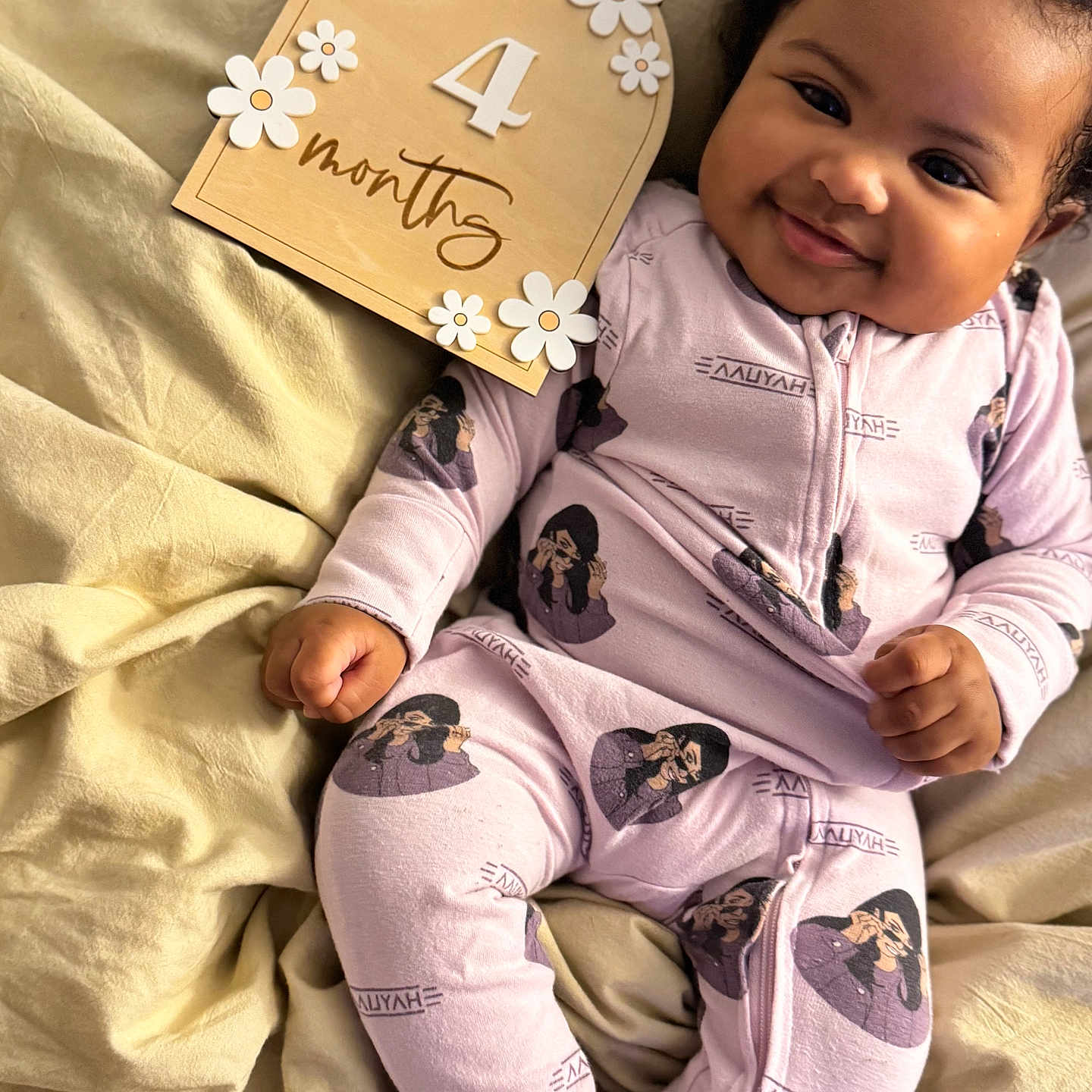 Somei Aliyah Madhoo is registered to the contest to win money with this photo: baby, blanket, child, clothing, cute, expression, face, flowers, hand, happy, indoors, infant, lying_down, milestone, onesie, portrait, skin, smiling, soft_lighting, wooden_sign