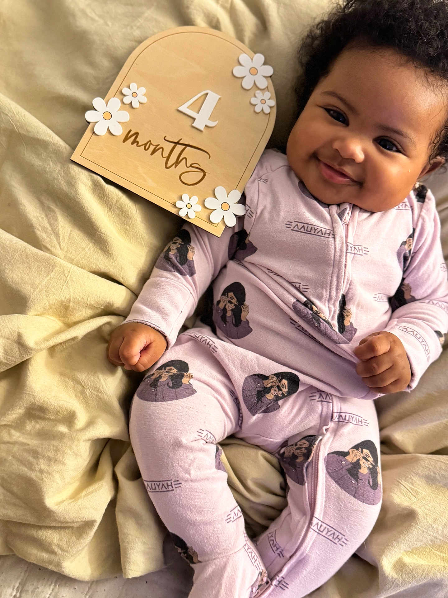 Somei Aliyah Madhoo is registered to the contest to win money with this photo: baby, smiling, infant, onesie, blanket, wooden_sign, flowers, milestone, cute, child, indoors, soft_lighting, happy, portrait, lying_down, clothing, hand, face, skin, expression