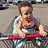 Zakai is registered to the contest to win money with this photo: toddler, child, shopping_cart, blanket, parking_lot, vehicles, sunlight, outdoor, curly_hair, smiling, retail_store, casual_clothing, footwear, hand, face, person, daytime, storefront, sporting_goods, urban