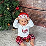 baby, child, christmas_tree, santa_hat, plaid_pants, white_rug, holiday, festive, decorations, ornaments, smiling, indoor, wooden_background, red, white, toddler, sitting, cute, happy, celebration