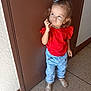 toddler, child, girl, red_shirt, blue_jeans, hair_bow, standing, brown_door, floor, sandals, curly_hair, casual_clothing, indoor, portrait, cute, pensive, young_child, fashion, person, full_body