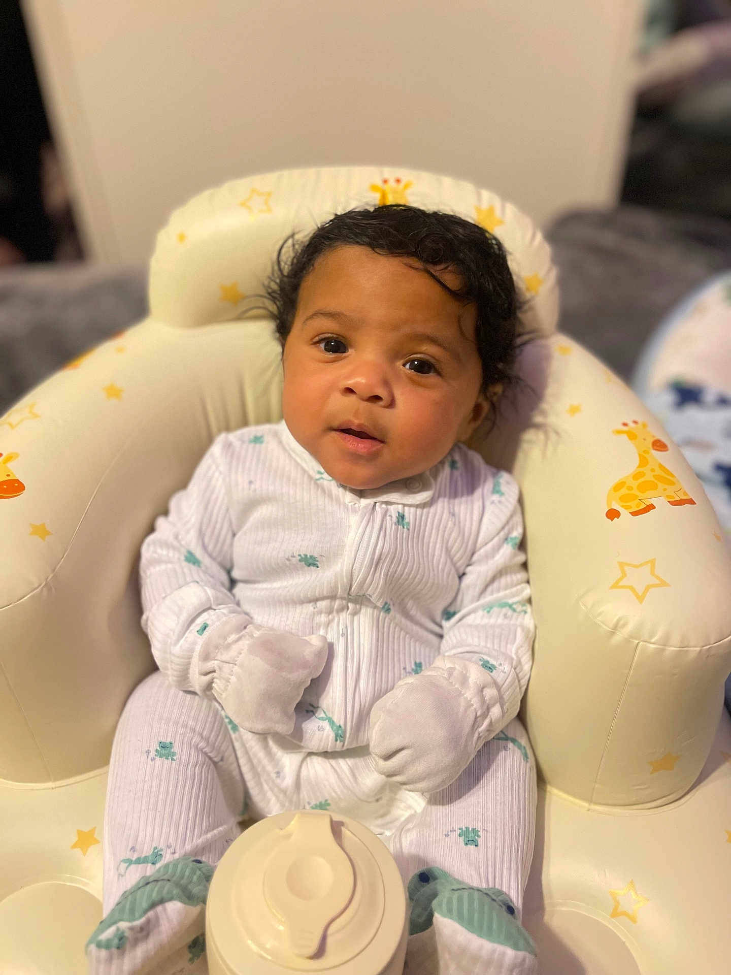 Achilles joined the competition — help win amazing prizes! baby, child, pajamas, white_clothing, mittens, seat, cushion, giraffe_pattern, stars, indoor, portrait, infant, cute, soft_lighting, face, looking_at_camera, sitting, cozy, young_child, adorable