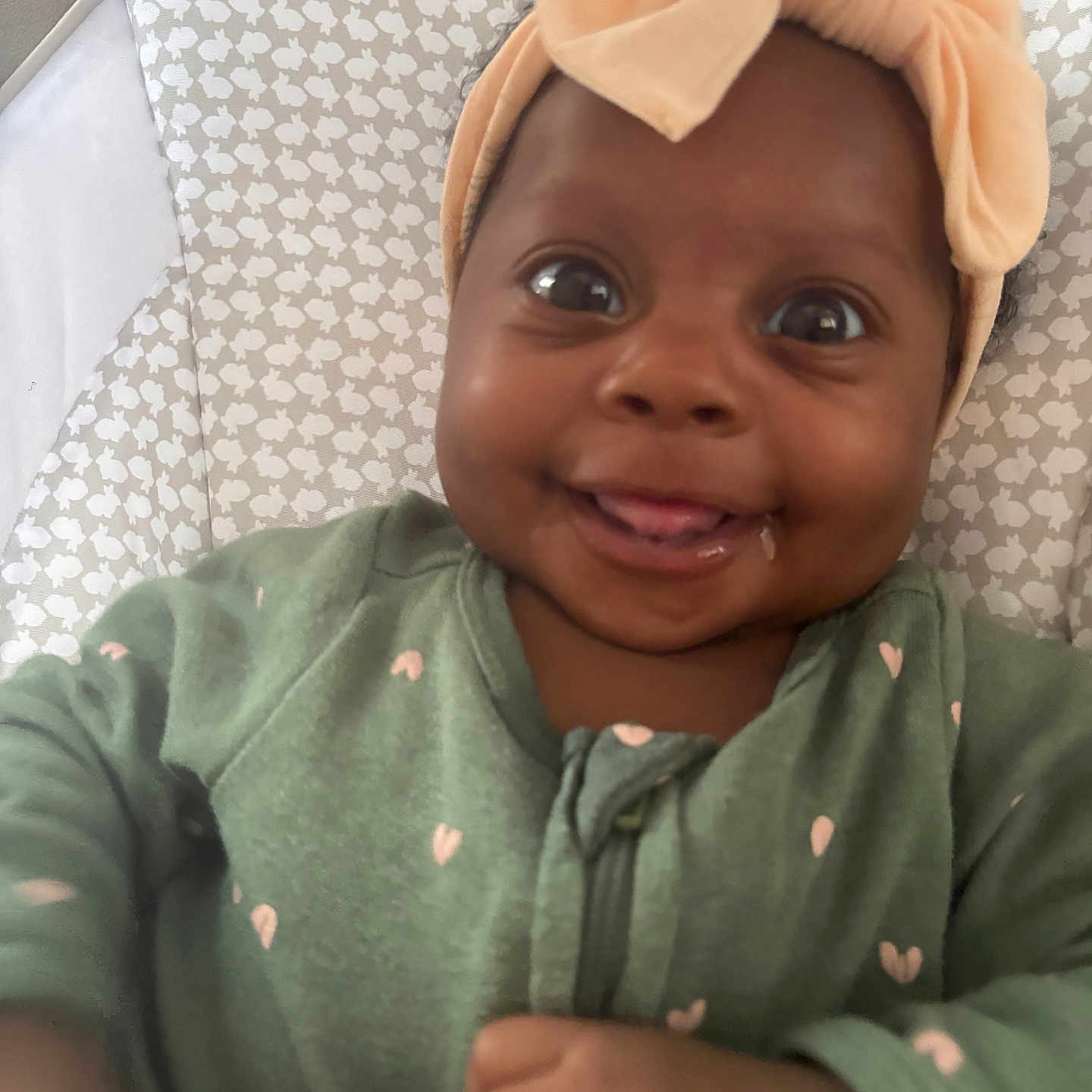 Elizabeth joined the competition — help win amazing prizes! baby, baby_clothes, child, closeup, cute, fabric, face, green_clothing, headband, indoors, infant, joyful, one_person, patterned_cushion, pink_hearts, playful, portrait, smiling, soft_lighting, tongue_out