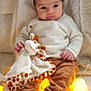 Basile a rejoint le concours — aidez-le/la à gagner de superbes lots ! baby, blanket, child, cozy, cute, expression, giraffe, indoor, infant, lights, pants, plushie, portrait, seated, socks, soft_texture, star_lights, sweater, toy, warm_colors