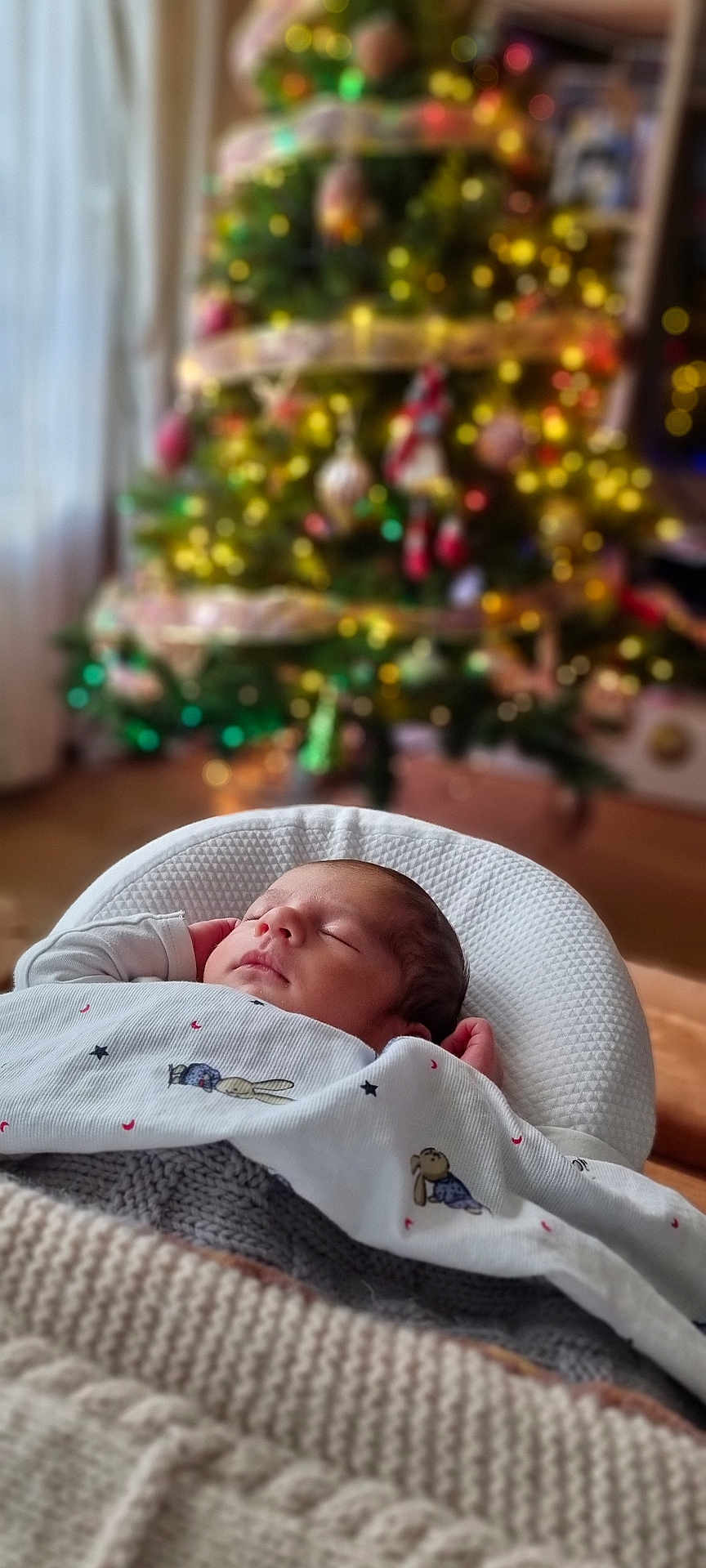 Basile a rejoint le concours — aidez-le/la à gagner de superbes lots ! baby, sleeping, blanket, christmas_tree, holiday, indoors, soft_light, cozy, infant, bokeh, decorations, festive, warm, knit, white_clothing, peaceful, portrait, cute, relaxation, home