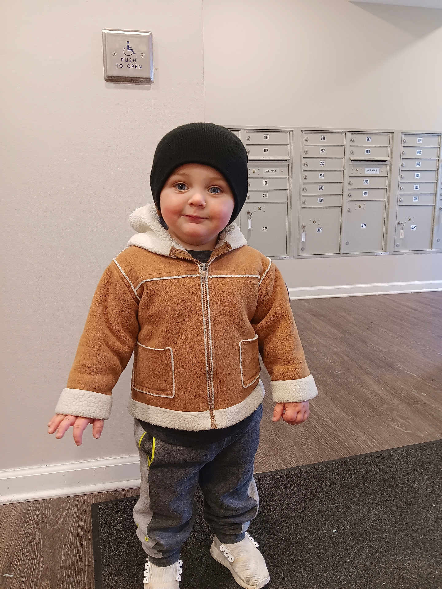 Jaxson is registered to the contest to win money with this photo: child, toddler, jacket, beanie, hat, sneakers, mailboxes, hallway, flooring, mat, indoor, person, clothing, cute, standing, smile, winter, cozy, young, casual