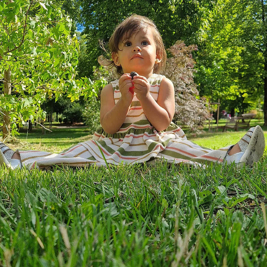 Thaïs participe au concours pour gagner de l'argent avec cette photo : blue_sky, child, curly_hair, cute, daylight, dress, grass, greenery, nature, outdoor, park, person, playful, shoes, sitting, summer, sunlight, toddler, trees, young_child